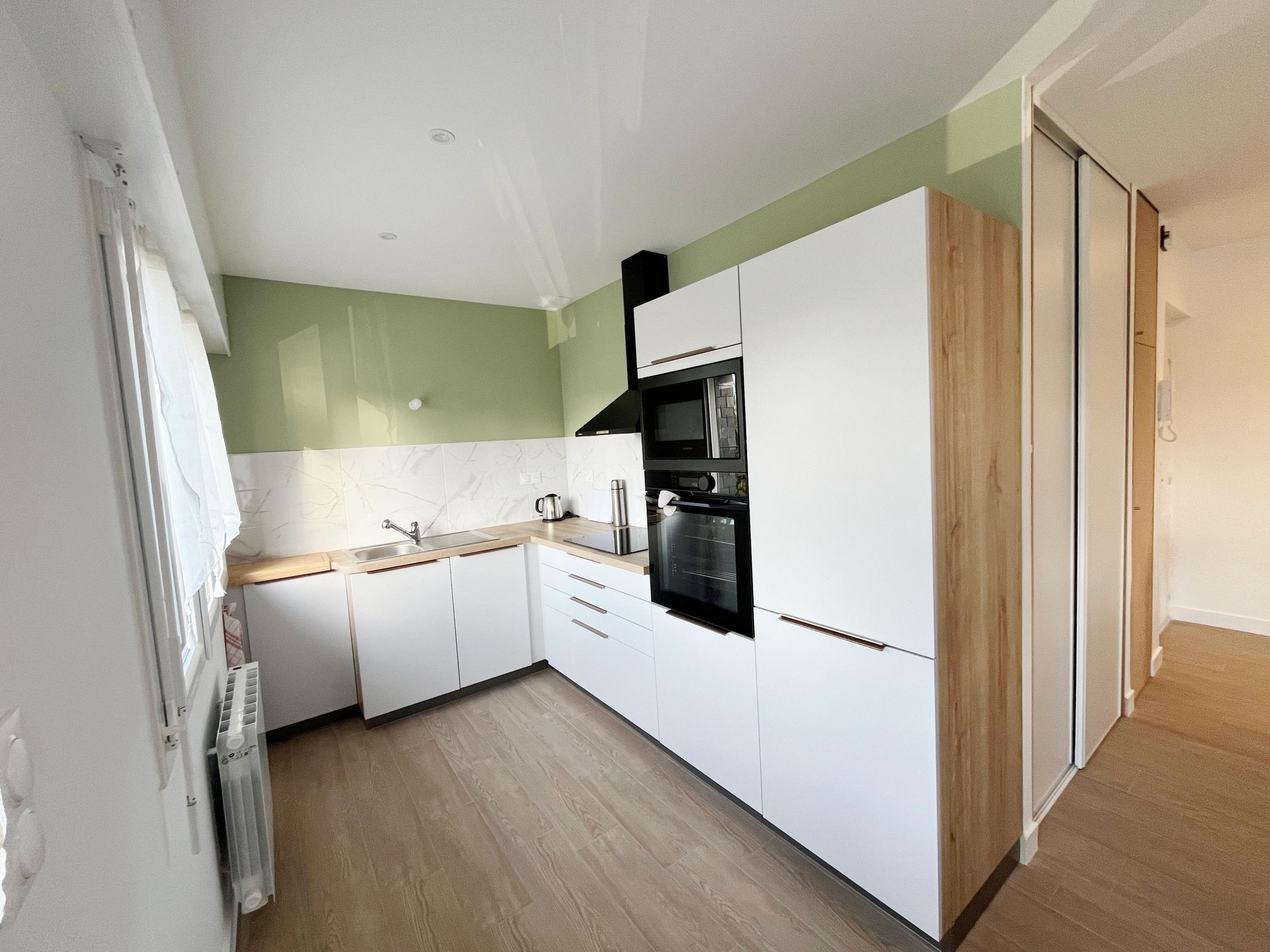 Een moderne keuken met witte kasten, een zwarte oven en een houten vloer.