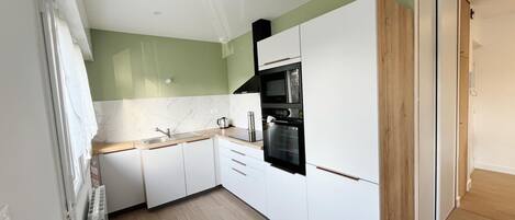 Een moderne keuken met witte kasten, een zwarte oven en een houten vloer.
