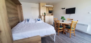 A bedroom with a bed, a desk, chairs, a television, and a small kitchen area. - BLUE OCÉANE - Studio rental Carnac swimming pool - U65 (Carnac)