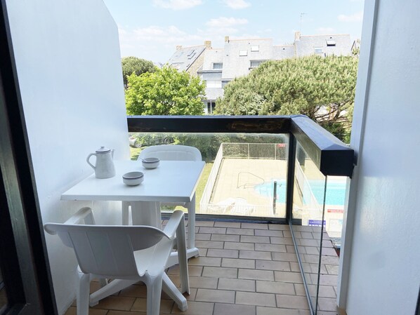 A balcony with a table and chairs, a pool, and a view of buildings and trees.