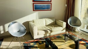 A living room with a white sofa, two framed pictures on the wall, a glass coffee table, and two floor lamps. - HORTENSIAS - Holiday apartment with sea view, facing the beach - T6 (Carnac)