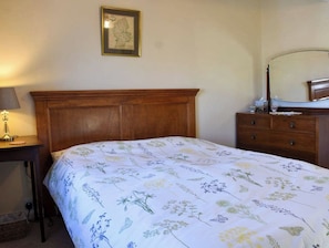 Une chambre à coucher avec une tête de lit en bois, une couvre-lit à motifs floraux, une table de chevet avec une lampe et une commode avec un miroir.