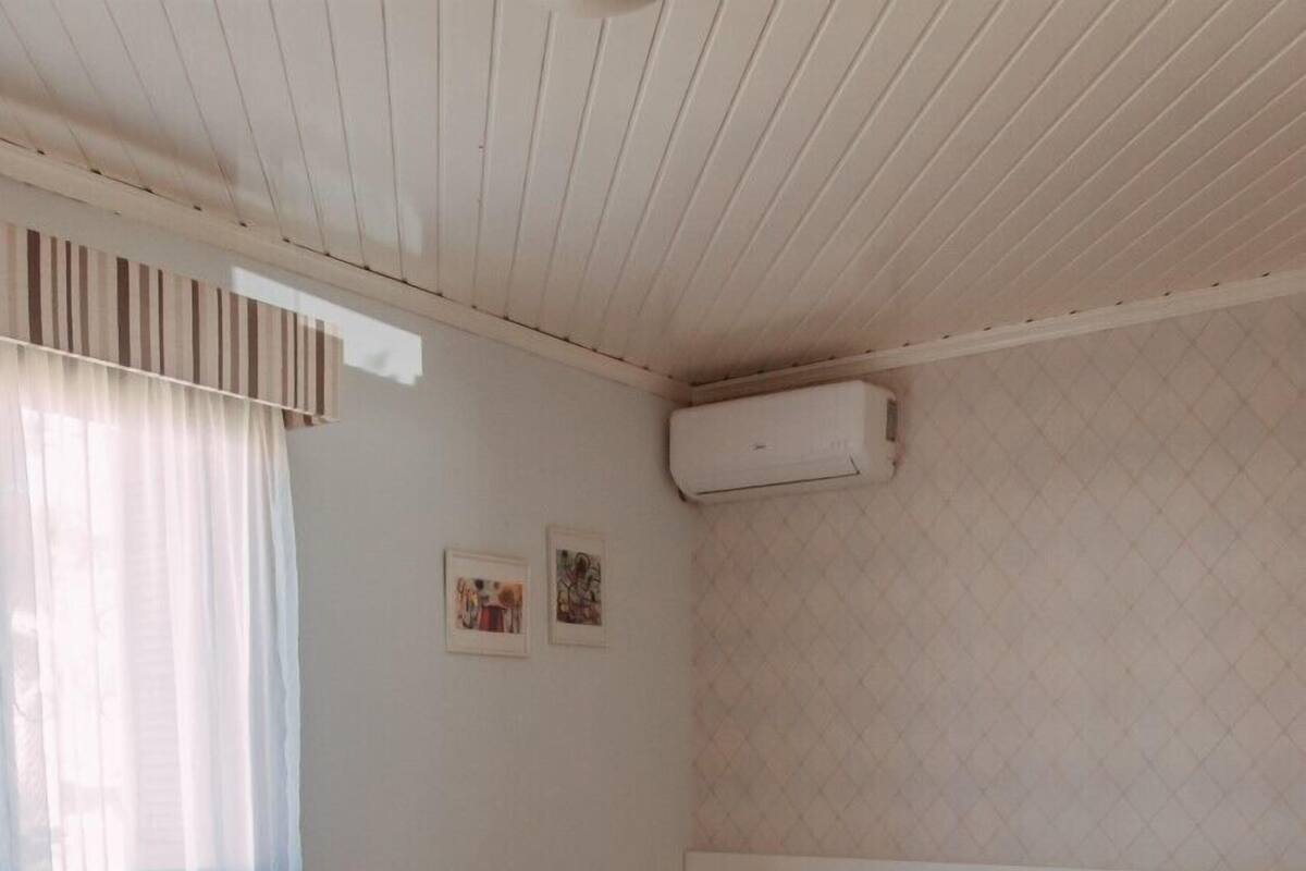 A hotel room with a bed, a radiator, a window with curtains, a wall-mounted air conditioner, and a patterned armchair.