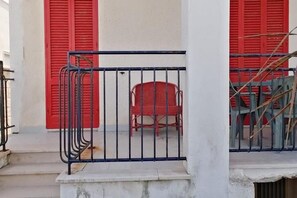 Uma varanda com guarda-corrimão de metal, uma cadeira vermelha e persianas vermelhas no edifício.