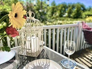 Ein Tisch draußen gedeckt mit einem Metalltisch, einem Weinglas aus Glas, einem weißen Teller und einem Vogelkäfig aus Metall mit Blumen.