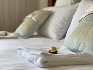 Ein ordentlich bezogenes Bett mit einem gefalteten weißen Handtuch und einem Schokoladenkuchen darauf.