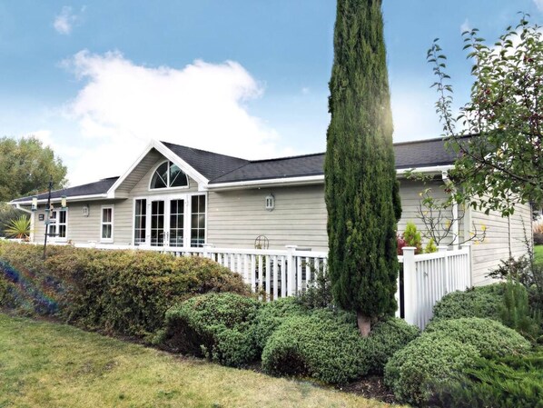 A two-story house with a white picket fence, a tall coniferous tree, and well-maintained shrubbery.