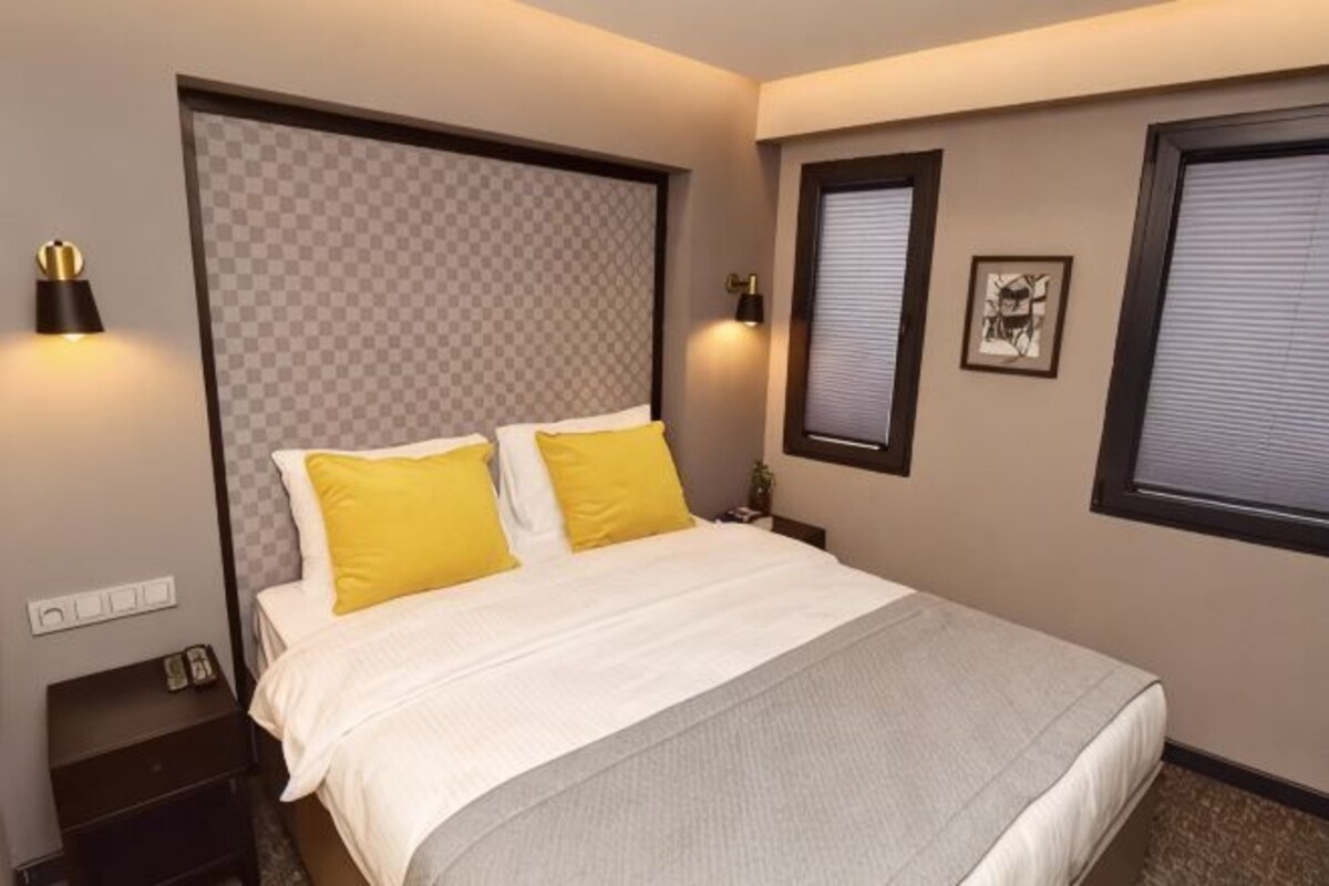 A hotel room with a large bed, two bedside lamps, a nightstand, and a window with blinds.