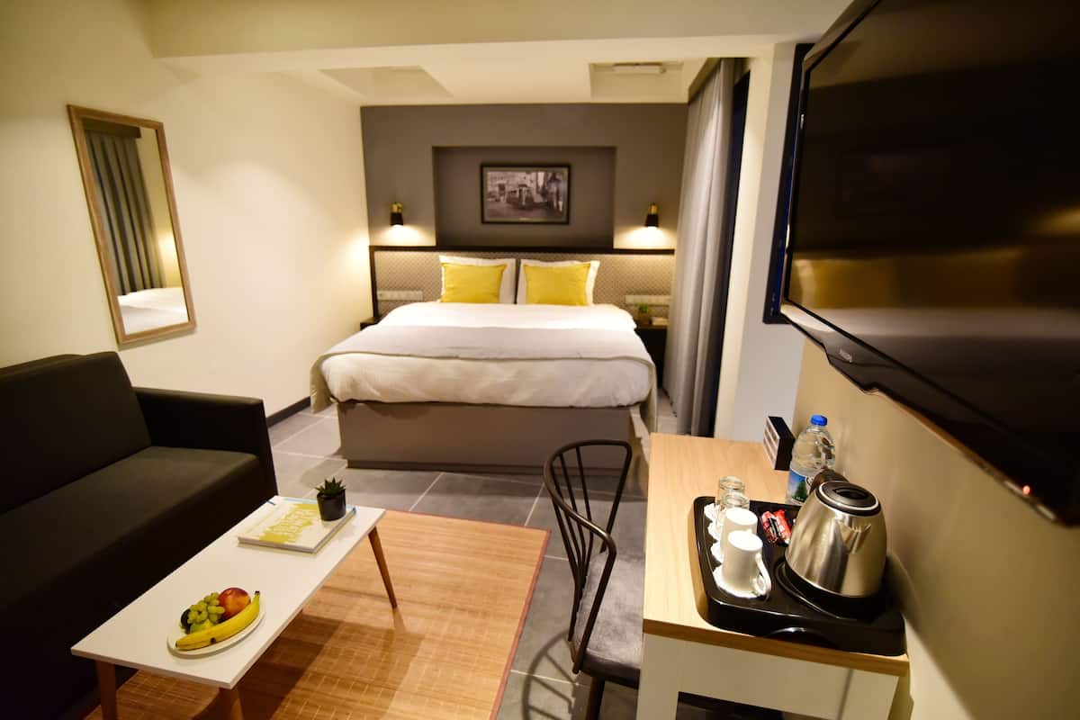 A hotel room with a bed, a desk with a kettle, a coffee maker, and a fruit bowl.