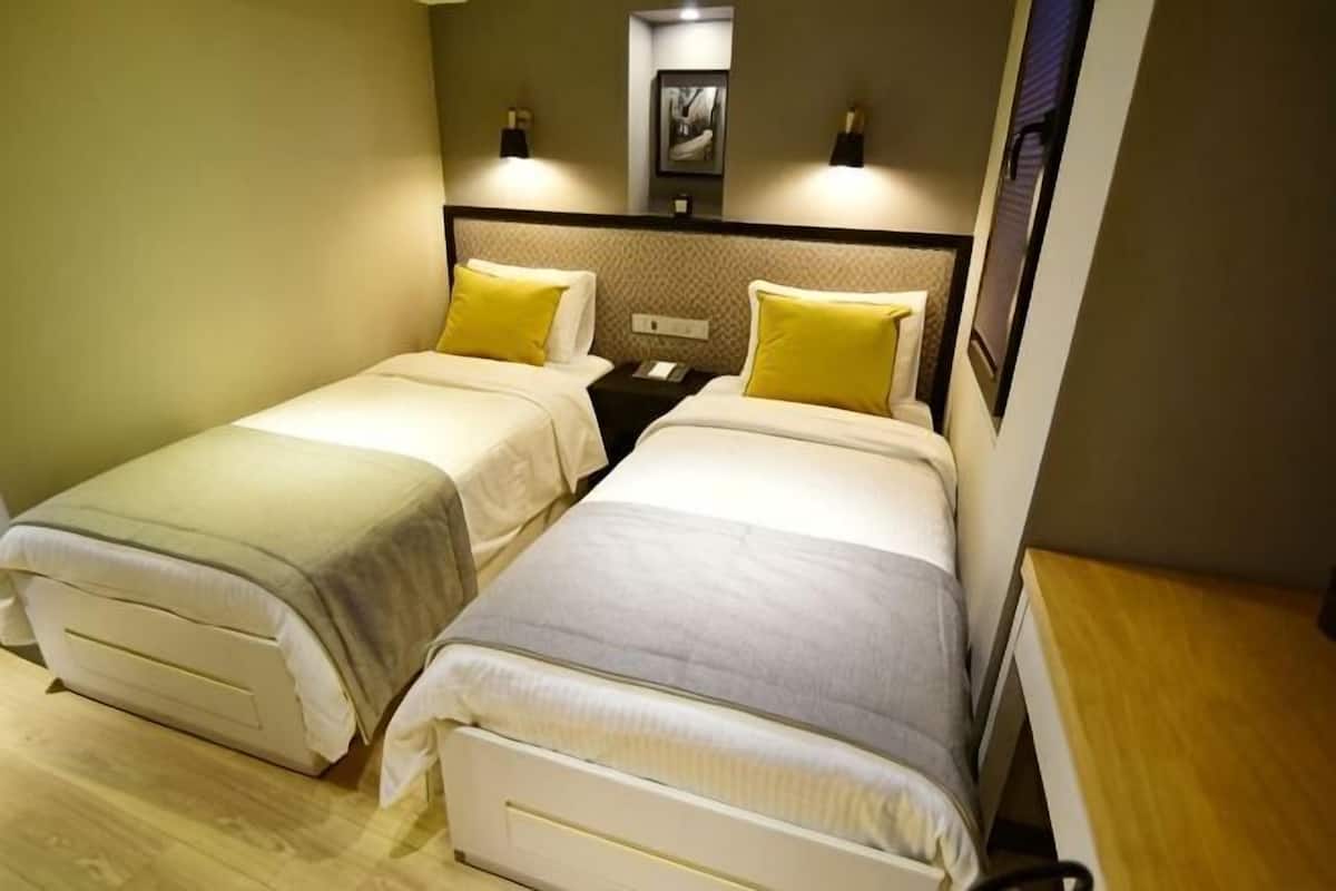 A hotel room with two beds, a nightstand, a wall-mounted TV, and a wooden side table.