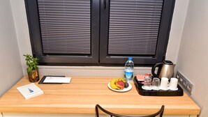 A wooden desk with a laptop, a book, a fruit plate, a water bottle, a kettle, and a cup set. - The Row Taksim Hotel (Istanbul)