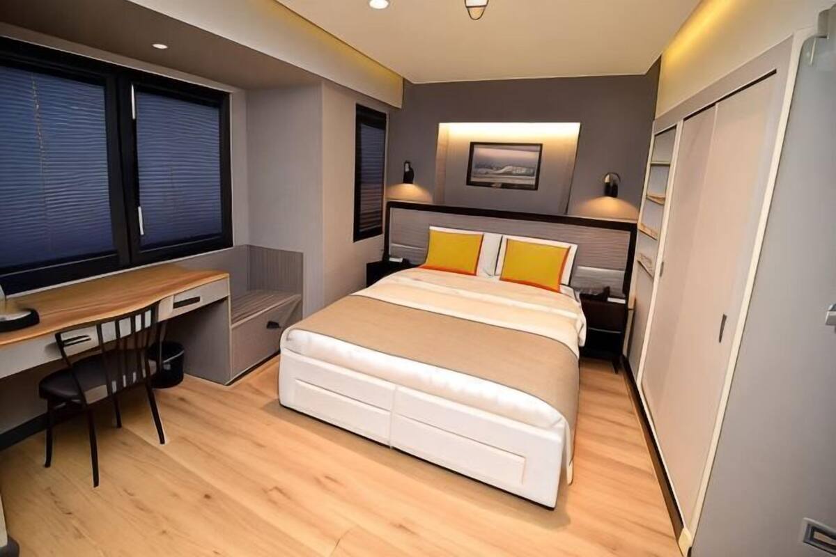 A bedroom with a bed, desk, chair, and a window.