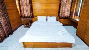 A neatly made bed with white linens, wooden headboard, and matching curtains. - Ruang Nyaman at Sukanagalih Resort (Cipanas)