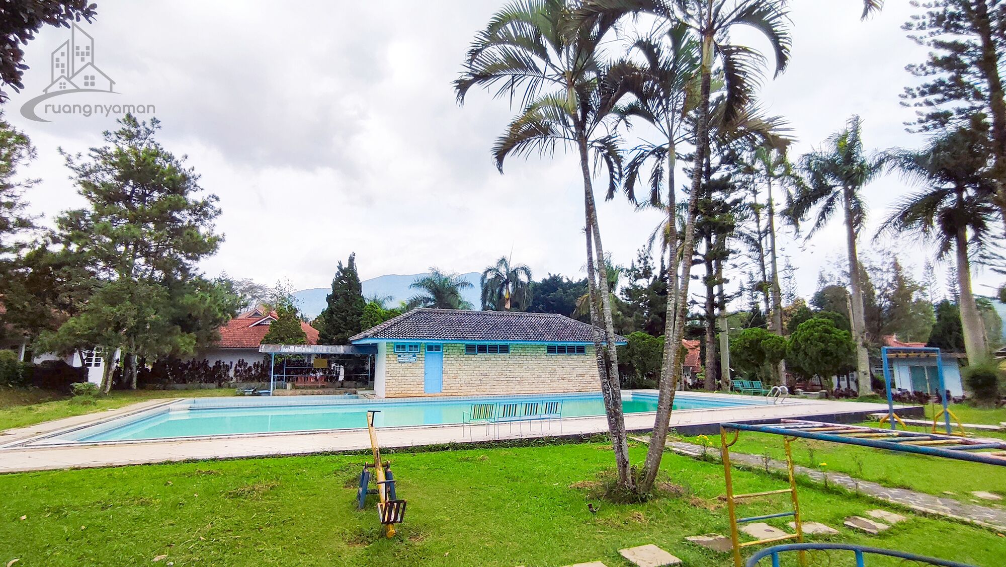 Une piscine avec, en arrière-plan, un bâtiment aux couleurs bleu et blanc, entouré de palmiers et de verdure.