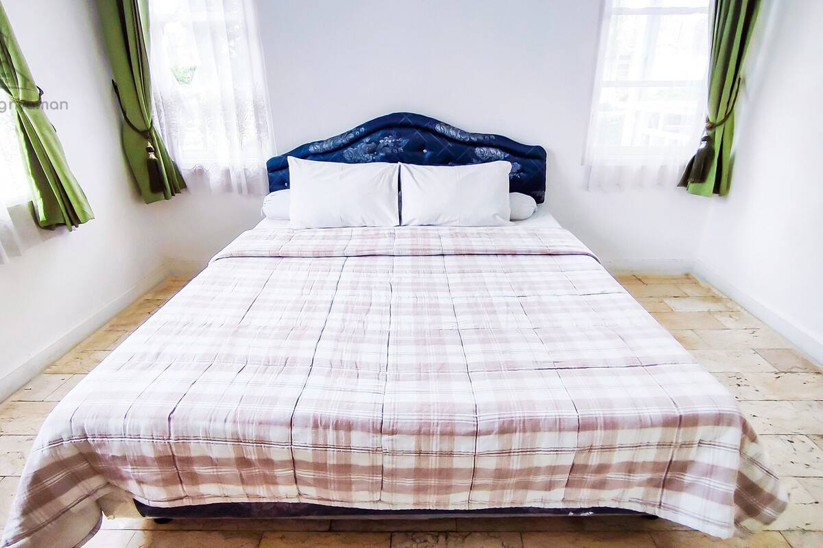 A neatly made bed with a plaid bedspread, a blue headboard, and white pillows.