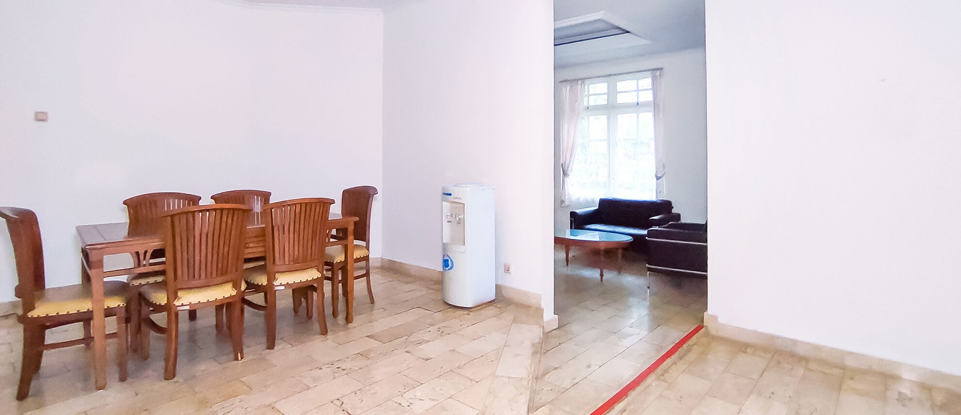 Un comedor con mesa y sillas de madera, un dispensador de agua y vistas a una sala de estar con sofá y mesa de centro.