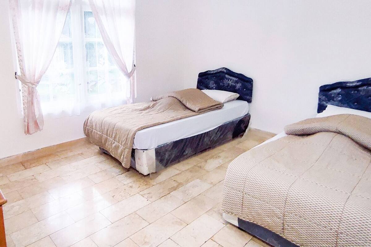 A room with two beds, a wooden dresser, and a window with sheer curtains.