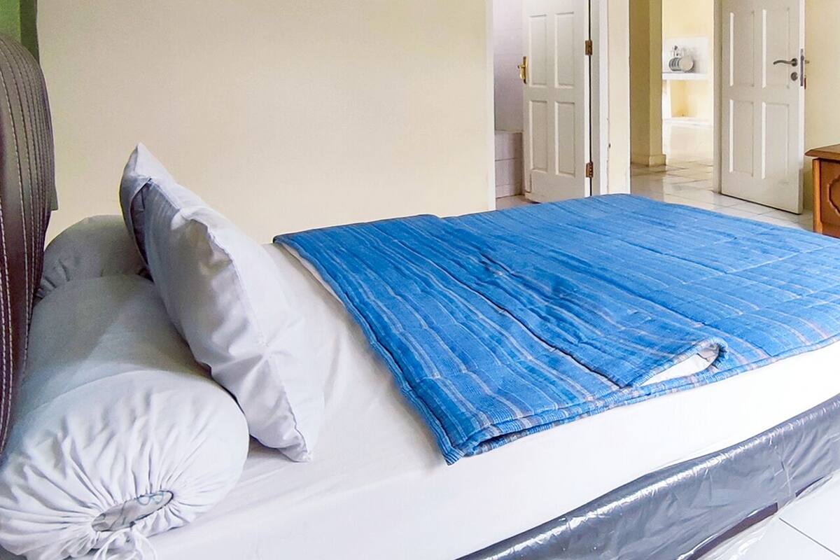 A bedroom with a bed covered in a blue blanket, a wooden dresser, and a mirror.