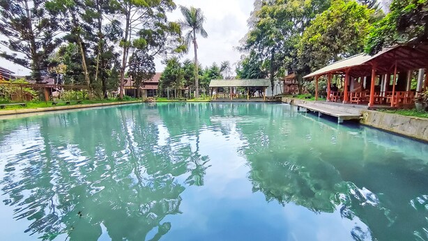 A clear swimming pool surrounded by trees and covered structures. - Ruang Nyaman at Sukanagalih Resort (Cipanas)