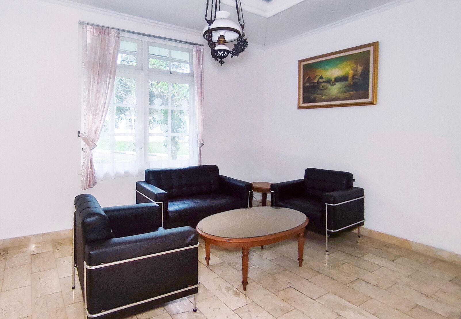 Ein Zimmer mit zwei schwarzen Ledersofas, einem Holztisch, einer Kristallleuchtre, einem Fenster mit Vorhängen und einem gerahmten Gemälde an der Wand.