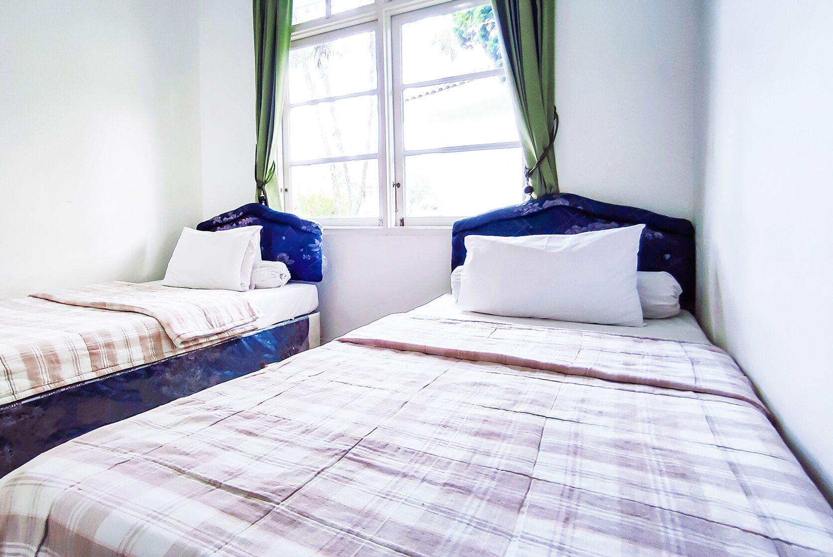 A room with two beds, each with a headboard, white bedding, and a window with green curtains.