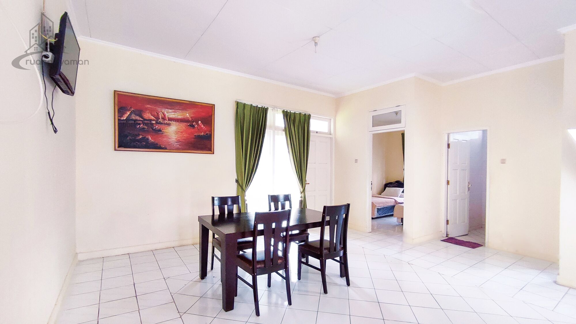 A dining area with a table and chairs, a painting on the wall, and a TV mounted on the wall.