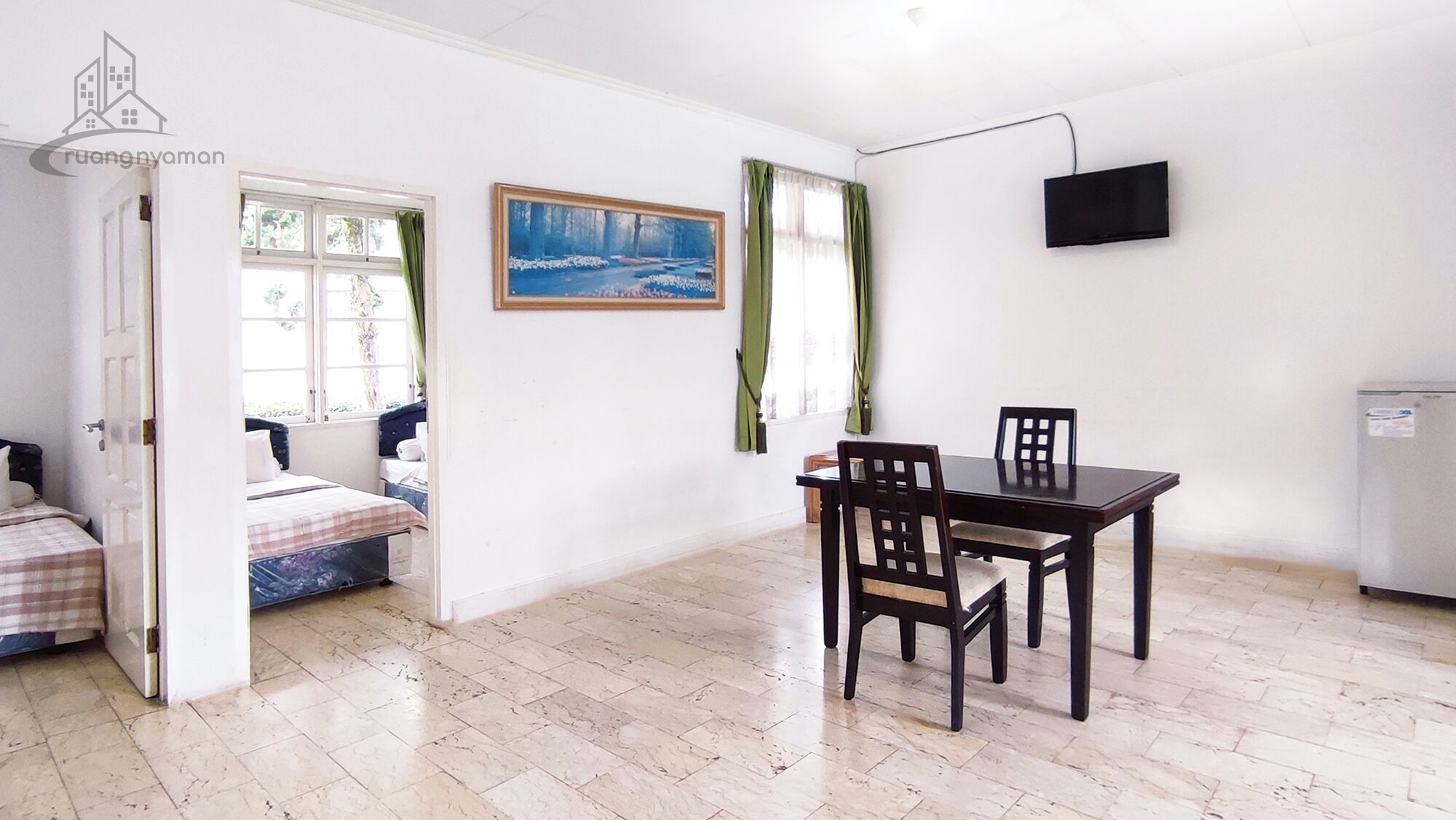 A room with a bed, a table with chairs, a painting, a TV, and a door leading to another room.
