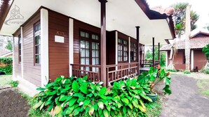 A wooden house with a porch, number K15, surrounded by lush green plants. - Ruang Nyaman at Sukanagalih Resort (Cipanas)