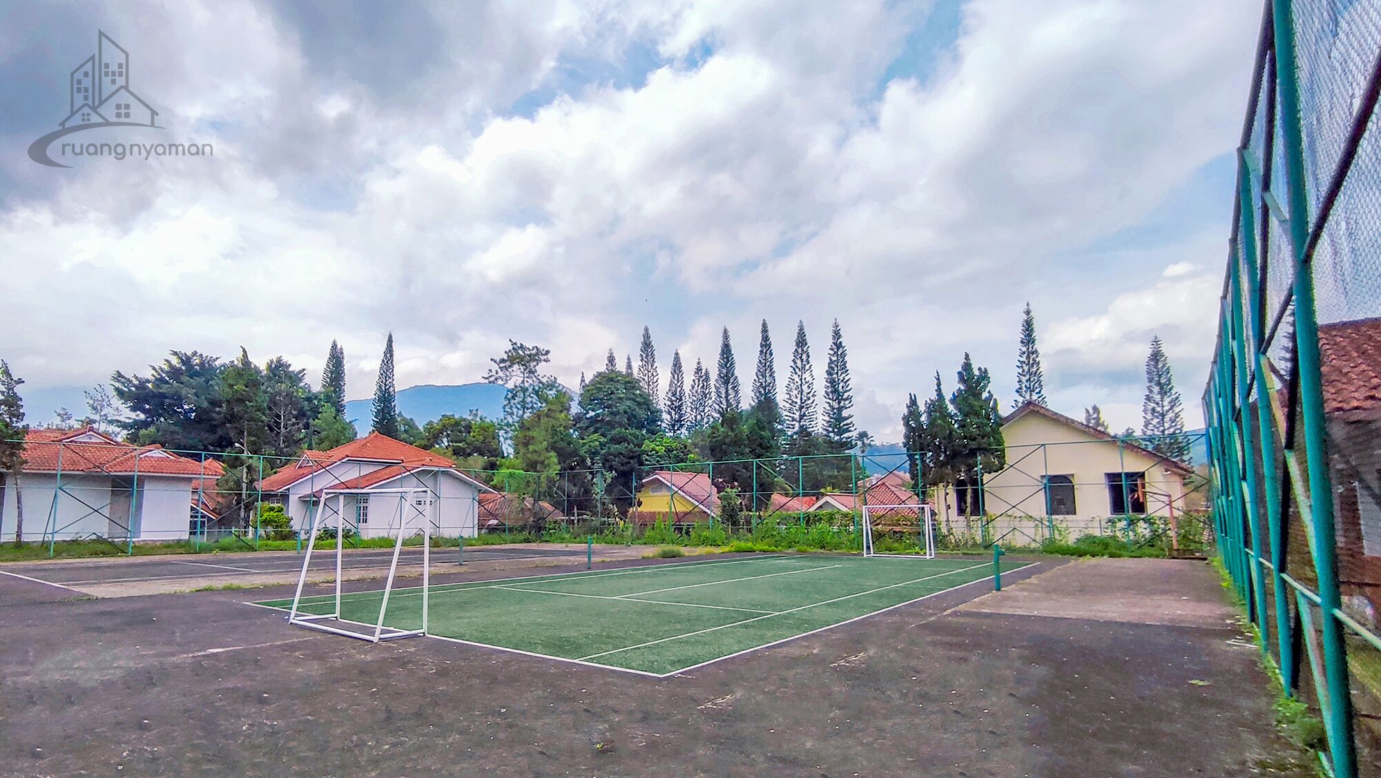 Una cancha de tenis exterior con red, rodeada de edificios residenciales y árboles.