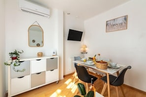 A modern dining area with a white table, black chairs, a white cabinet with drawers, a wall-mounted TV, and a framed artwork.