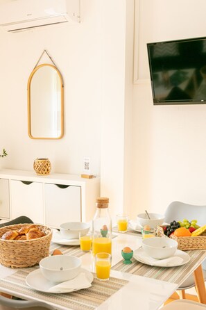 Un desayuno con una mesa para dos, incluyendo platos, tazones, una cesta de croissants y una botella de jugo de naranja.