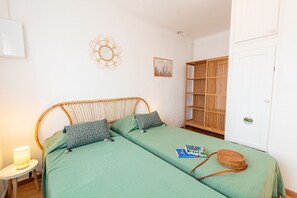 A room with a bed, a small table with a lamp, a bookshelf, and a door.