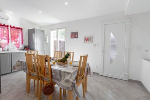 A modern kitchen with white cabinets, a dining area with a table set for two, and a door with frosted glass panels. - La Janette, a charming villa near the sea (Hyères)