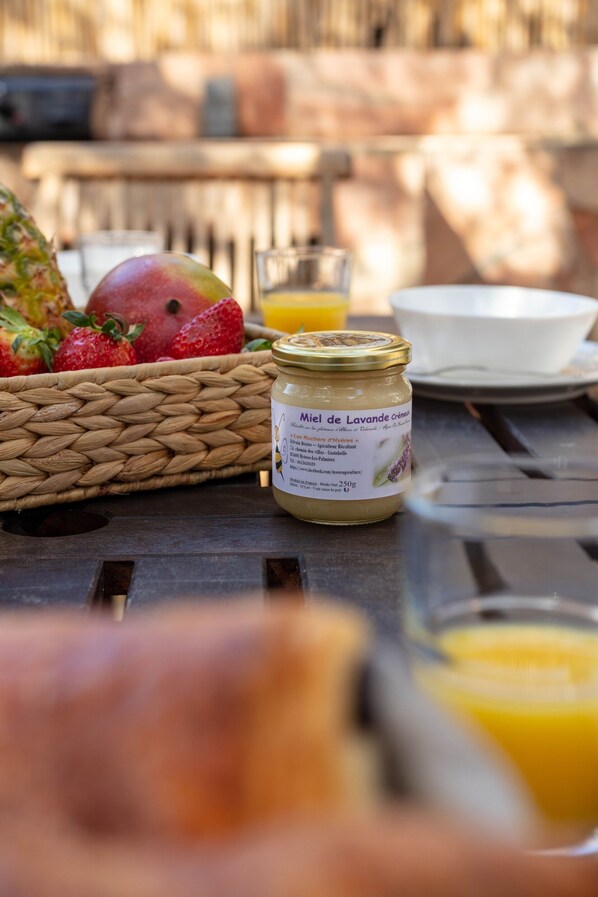 A wicker basket filled with fruits, a jar of honey, a glass of orange juice, and a white bowl on a wooden table.