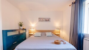 Une chambre à coucher comprenant un lit, des tables de chevet, une commode, une lampe fixée au mur et une fenêtre avec des rideaux.