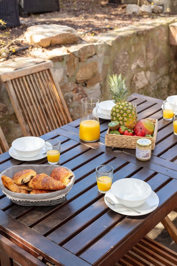 A wooden table set for breakfast with croissants, fruit, and orange juice. - La Janette, a charming villa near the sea (Hyères)