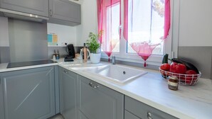 Une cuisine moderne avec des meubles gris, un plan de travail blanc, un évier et une fenêtre agrémentée de rideaux roses.
