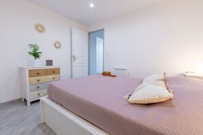 Um quarto com uma cama, uma cômoda, um vaso de plantas e uma porta que dá para outro ambiente.