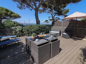 An outdoor patio with wicker furniture, a grill, and a view of the sea.