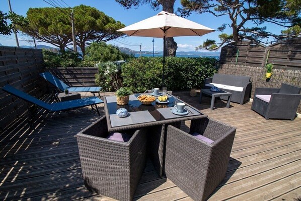 An outdoor patio with wicker furniture, a table set with plates, cups, and a fruit bowl.