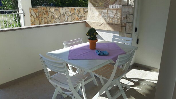 Une table et des chaises en plastique blanc sur un balcon, avec un mur en pierre et un portail en métal en arrière-plan.