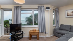 A living room with a TV, a small table, a sofa, and a view of the outdoors. - Amazing Sea Views from this Ground Floor 2 Bedroom High Spec Apartment (Torpoint)