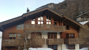 A wooden chalet with a balcony, surrounded by snow and trees. - Haus Bärgbach by Zermatt Premium Apartments (Zermatt)