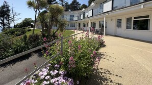 A modern two-story building with a covered patio area, surrounded by landscaped gardens and a variety of plants.