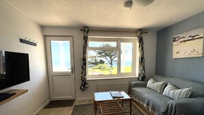 A compact living room with a television, a sofa, a small table, and a window with curtains.