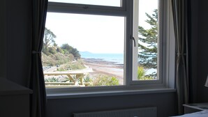 Een slaapkamer met uitzicht op een strand en een picknicktafel buiten het raam.