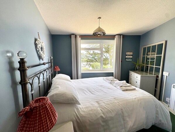 A bedroom with a bed, a dresser, a window with curtains, a ceiling light, and a wall with a mirror and signs.
