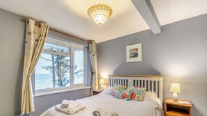 Ein Schlafzimmer mit Bett, Nachttisch, Lampe, einem Fenster mit Vorhängen und einem Bild an der Wand.