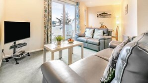 A modern living room with a sofa, a coffee table, and a flat-screen TV. - Cornish Apartment with Private Balcony & Stunning Sea Views (Seaton)