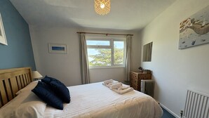 Een slaapkamer met een groot bed, een houten hoofdbord, een nachtkastje met een lamp, een radiator en een raam met gordijnen.